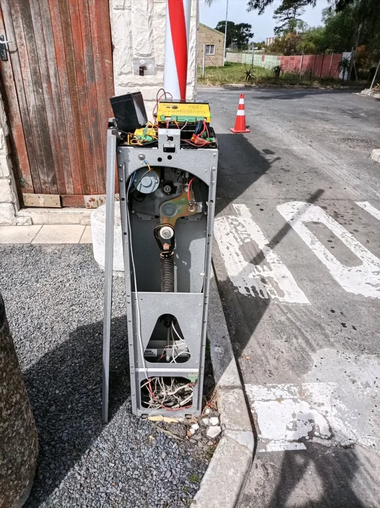 Boom gate at a vehicle entrance with its barrier arm raised and cabinet open for servicing.